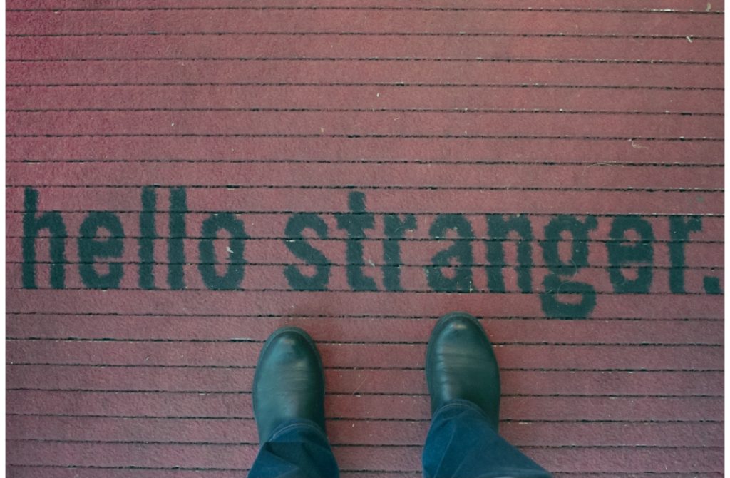 A person standing on a doormat that reads ‘hello stranger,’ symbolizing how people instinctively feel comfortable opening up and sharing personal stories.