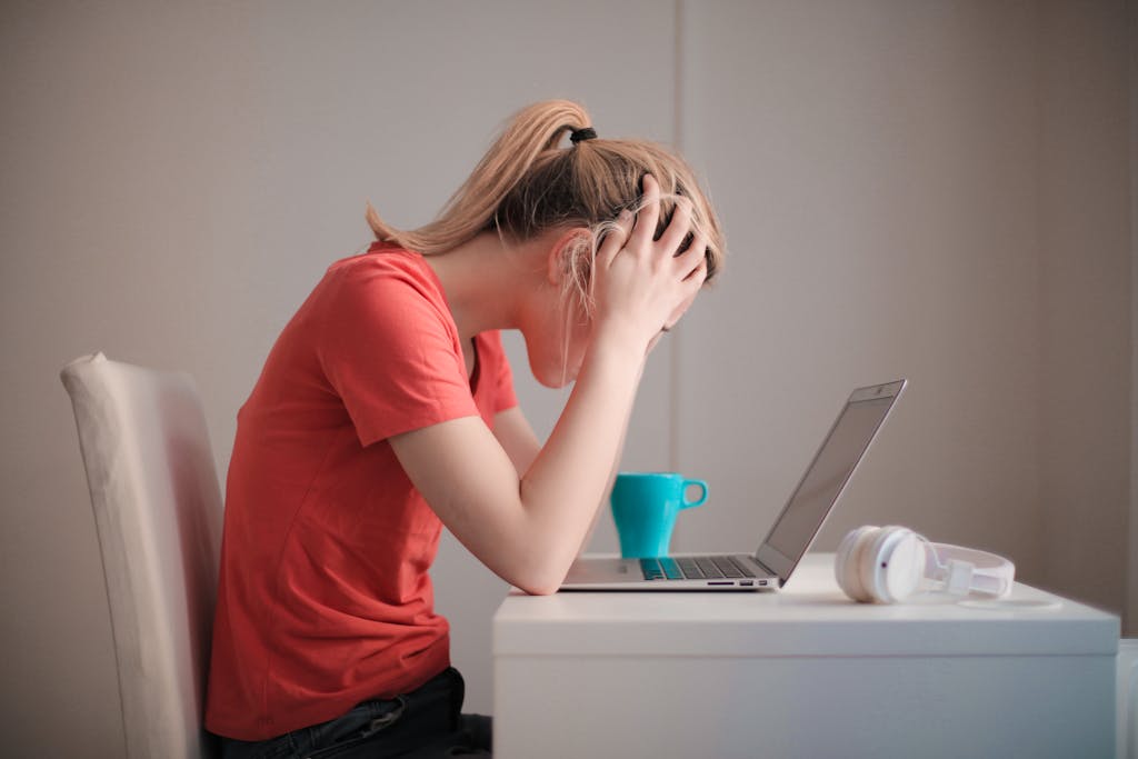 Young woman feeling stuck while studying at home with a laptop and coffee cup.