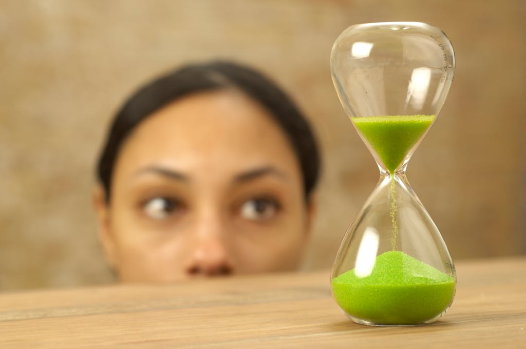 A focused woman looks at an hourglass with vibrant green sand. Concept of time and patience.