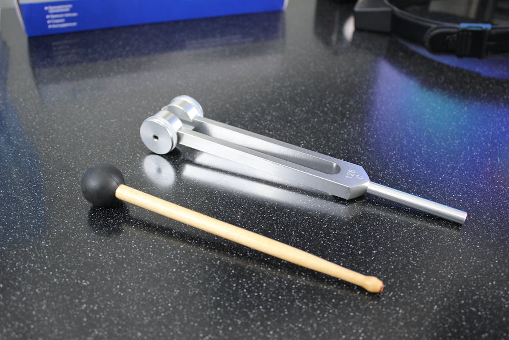 sound wave therapy benefits using a shiny metal tuning fork with mallet on speckled black table, for sound therapy or music.