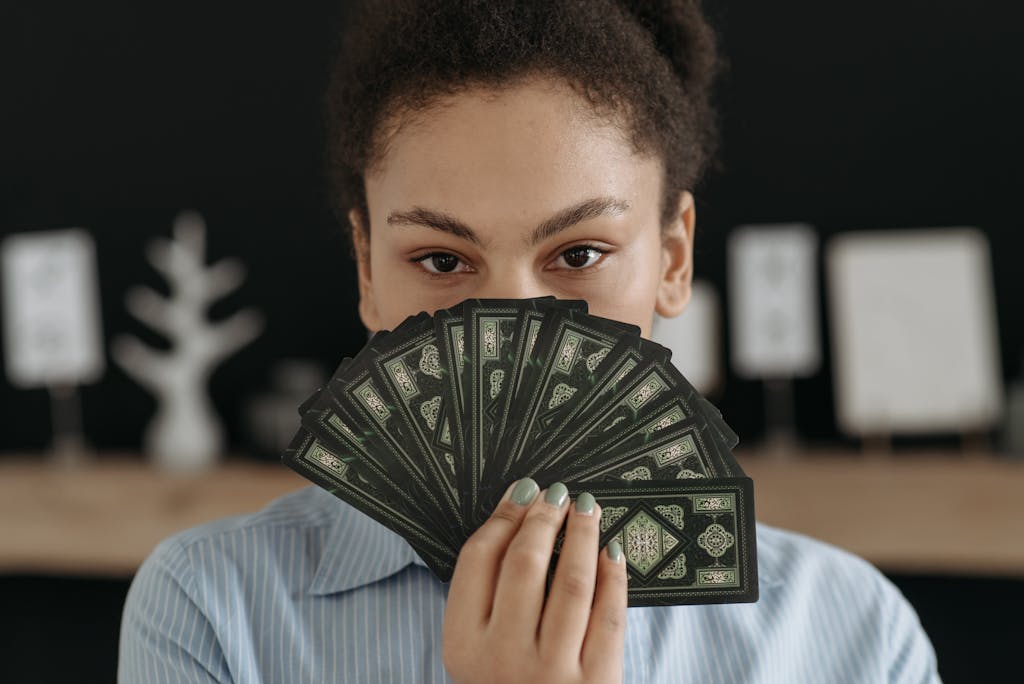 A woman with a focused expression holding a fan of tarot cards, conveying mystery and reflection.