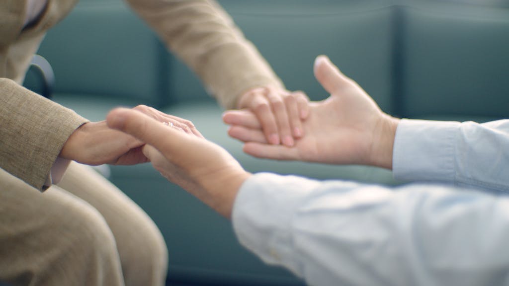 Close-up of two people holding hands, symbolizing support and compassion in a peaceful setting.
