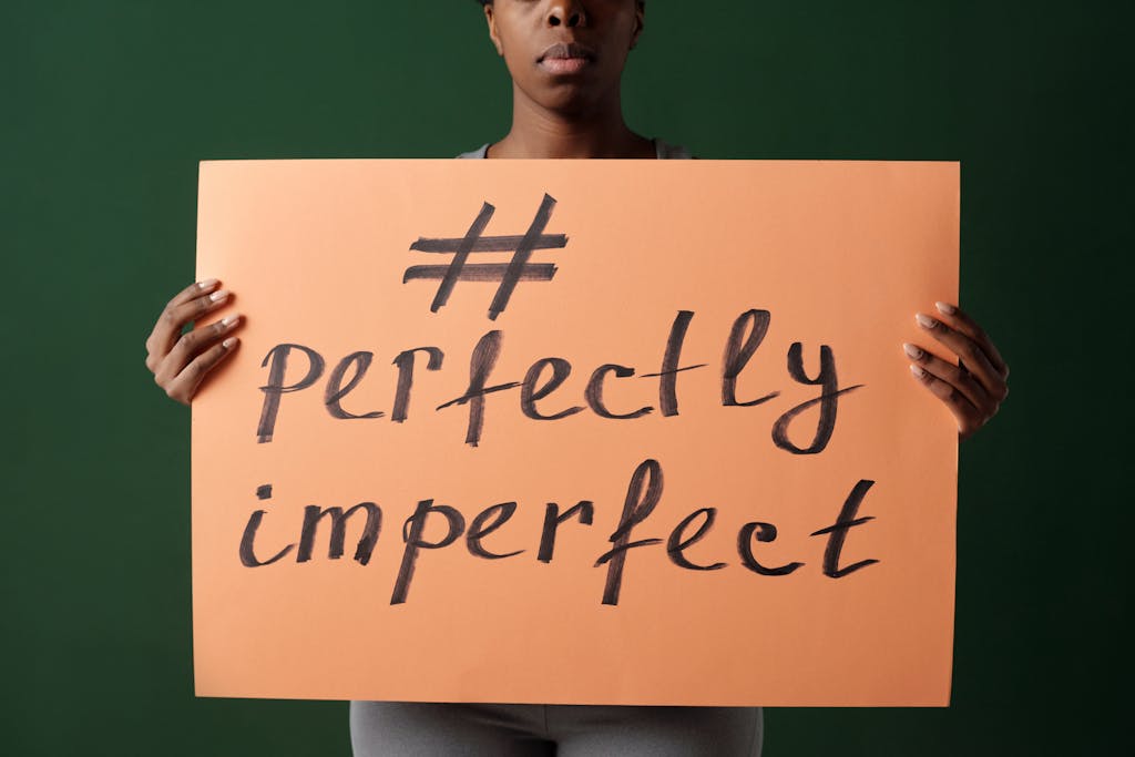 A woman holds a sign with 'perfectly imperfect' written on it, reflecting self-acceptance.
