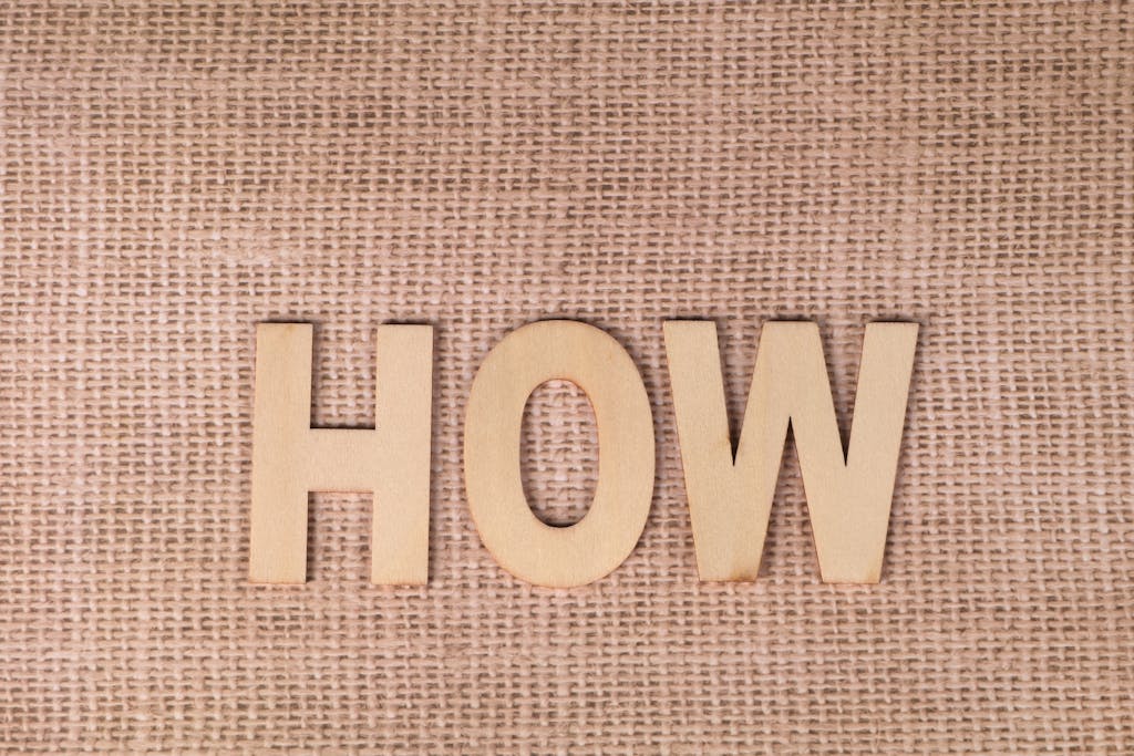 Word 'HOW' formed with wooden letters on textured burlap surface.