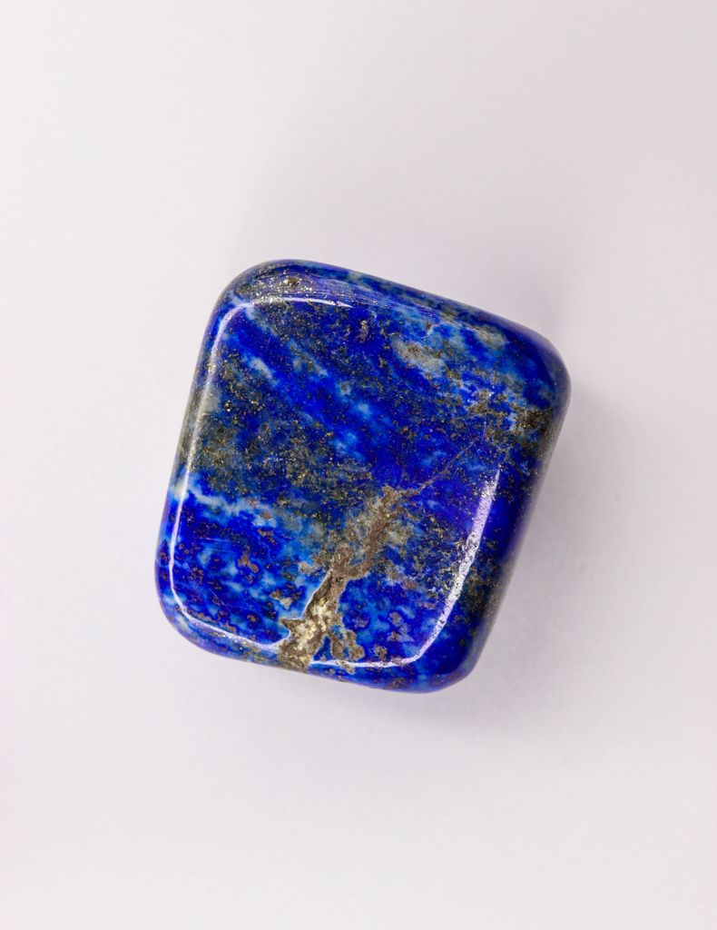 Close-up of a polished Lapis Lazuli gemstone showcasing vibrant blue hues on a white surface.