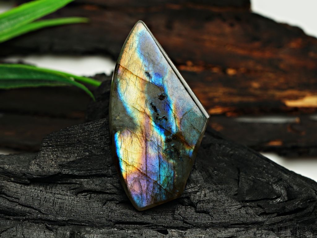 Stunning iridescent labradorite gemstone displaying vibrant colors on textured dark wood.